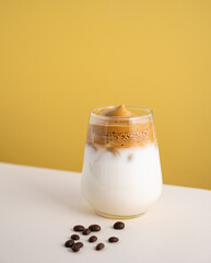 Dalgona coffee with milk in a glass with ice cubes and grains on a yellow background. The concept...