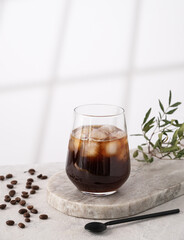 Iced coffee in a glass with ice cubes and grains on a light marble background with morning shadows. The concept of a cold summer drink. Copy space