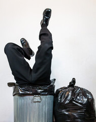 Businessman in Suit Stuck in Trash Can With Legs Sticking Out. Concept of Over a Barrel. Businessman Thrown Away by Capitalism and Greed.