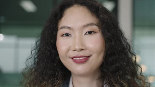 Closeup face headshot of Asian stylish woman attractive tourist is standing smiling and looking at the camera. Portrait of female traveler confident with long curly hairstyle waiting in airport lounge