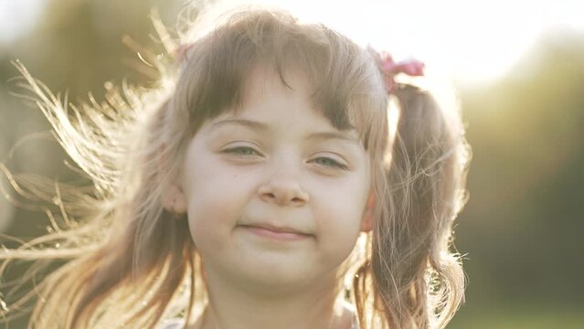 Happy girl in the sun in wind. Close-up of the girl face in the park. Dream girl. Hair in the wind. The child smiles at the camera. Girl's dream. Face close-up. Happy child in the park. Beautiful face