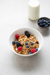 White bowl with granola and fresh berries and milk