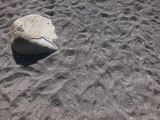 Volcanic black sand from the beach at Hilo, Hawaii. Gray rock with a hard shadow in the upper corner. Richardson Beach Park.