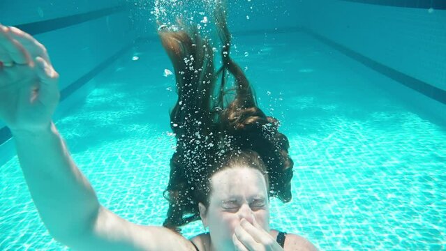Blue swimming pool, underwater shooting, sunny day. Chubby girl drowns in water. Slow motion