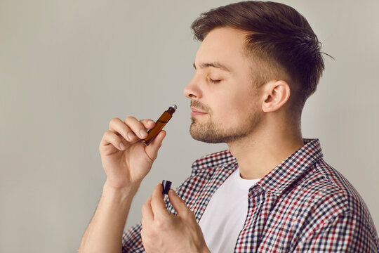 Happy young man smelling good quality essential oil. Side view portrait of handsome man holding roller bottle to his nose and enjoying wonderful scent of natural essential oil. Aromatherapy concept