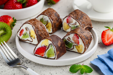 Chocolate dessert rolls with fruits. Rolled chocolate crepes with ricotta and strawberry, kiwi and banana. Sweet sushi. Selective focus