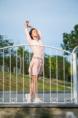 Woman in pink dress standing on river bank with hair flying on wind, blue sky background.