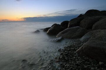 Orange sunset over the ocean with smooth waves and stones in water. Long exposure seascape
