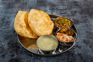 Traditinal punjabi desi lahori nashta Bhaturay Channay with raita, achaar and salad served in thali isolated on dark background side view of channay puri breakfast platter