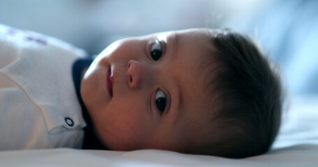 Cute baby toddler lying in bed looking at camera portrait