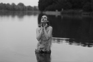 Young woman in wet dress swimming in the lake in black and white