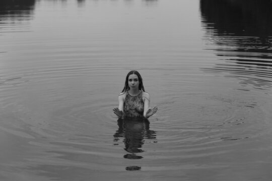 Young woman in wet dress swimming in the lake in black and white