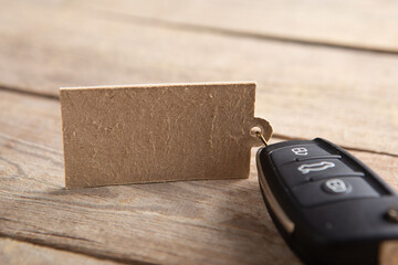 Fototapeta premium Car insurance or rent concept. Vehicle security key with blank tag on the wooden background