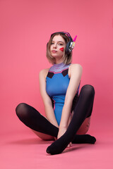 sexy gamer girl in a revealing bright bodysuit and gaming headset on a pink background © rotozey