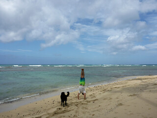 Man does Handstand on Diamond Head beach with black dog