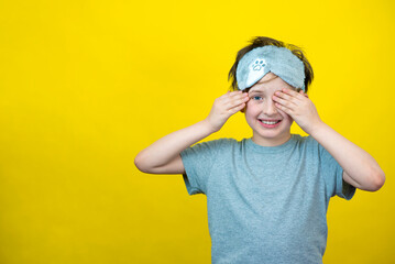 A smiling little boy  in a fashionable accessory sleep mask. yellow background