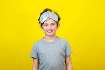 A smiling little boy  in a fashionable accessory sleep mask. yellow background