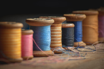 Fototapeta na wymiar Seven old wooden spools of thread in different colors in retro and vintage style in soft contrasted light