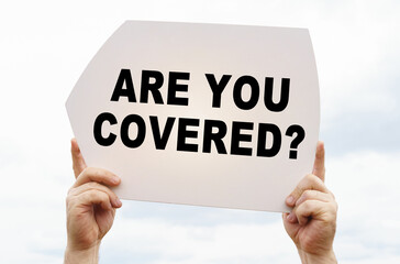 Against the background of the sky in the hands of a man is a sign with the inscription - ARE YOU COVERED