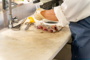 Unrecognizable fishmonger cleaning the fish with water after cutting it on a white table next to the cutting utensils. High quality photo