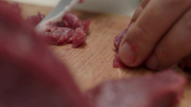 Close-up chef male cuts a juicy red piece of beef meat on a wooden board with a large kitchen knife in the kitchen.