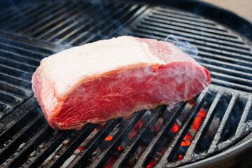 Raw dry aged wagyu roast beef steak grilled as close-up on a charcoal grill with fire and smoke