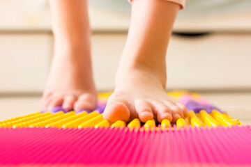 Closeup little girl's feet on orthopedic massage mat. Foot massage for child.