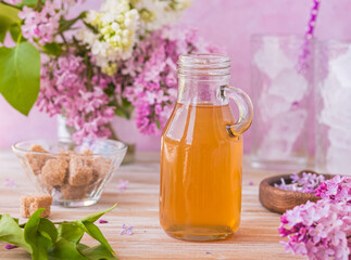 Lilac flavored sugar syrup for lemonades, ice cream or biscuits in a glass bottle on a light wooden background.