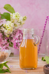 Lilac flavored sugar syrup for lemonades, ice cream or biscuits in a glass bottle on a light wooden background.