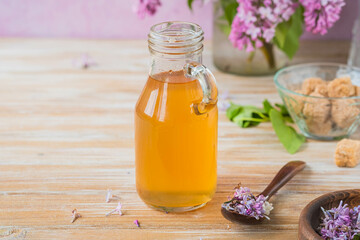 Lilac flavored sugar syrup for lemonades, ice cream or biscuits in a glass bottle on a light wooden background.