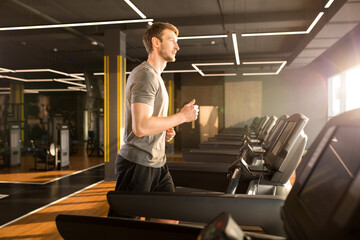 Young man in sportswear running on treadmill in front of window in gym