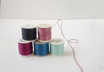 Five Spools of Cotton Sewing Thread in Differnt Colors with Threaded Needle on White Canvas Background