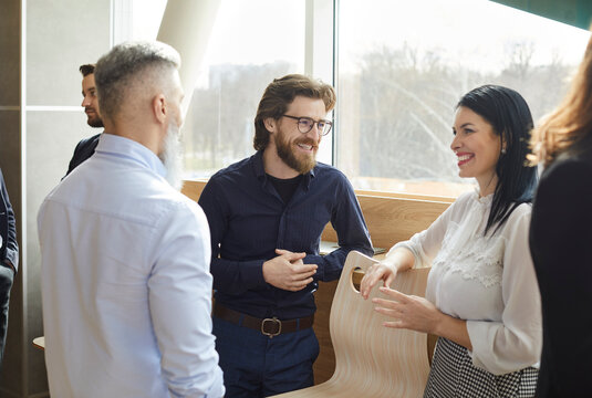 Business colleagues having fun chatting and discussing work in casual conversation in office. Beautiful business men and woman in stylish business attire smiling joking and discussing work.
