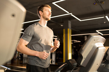 Young smiling man in sportswear running on treadmill in sports club