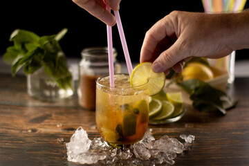  finishing a cocktail with liqueur by looking at the bartender's hands, ice around the glass, limes, good herb, cane sugar with a black bottom.