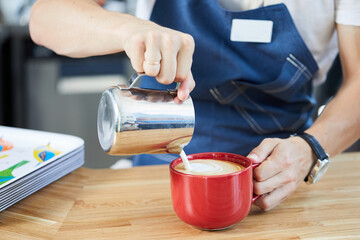 barista's hands pouring milk into a cup of cappuccino