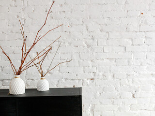 a white ceramic vase with dry branches on a black pedestal against a white brick wall. Interior