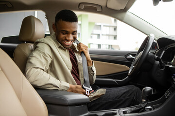 African American man sitting in a car in a car dealership fastening his seat belt