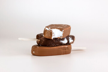 Chocolate ice cream bar with sticks. Melting and broken chocolate popsicles on pastel color background. Refreshing Summer dessert close up image.