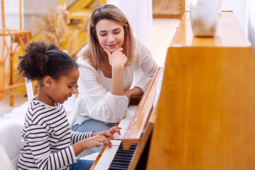 Woman and girl playing a piano. Beautiful mom teaching her daughter playing a piano. The piano...
