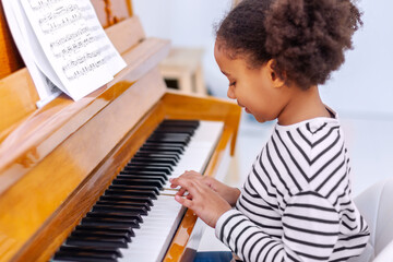 Young little student pianist, at home taking piano lessons. Pretty girl learning and practicing the...