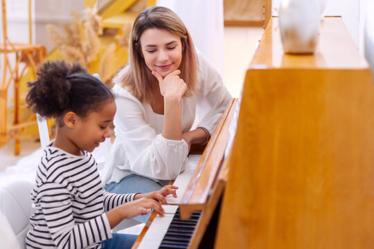 Woman and girl playing a piano. Beautiful mom teaching her daughter playing a piano. The piano teacher experienced pianist gives classes to a young little student. Hobby and activity for the children.