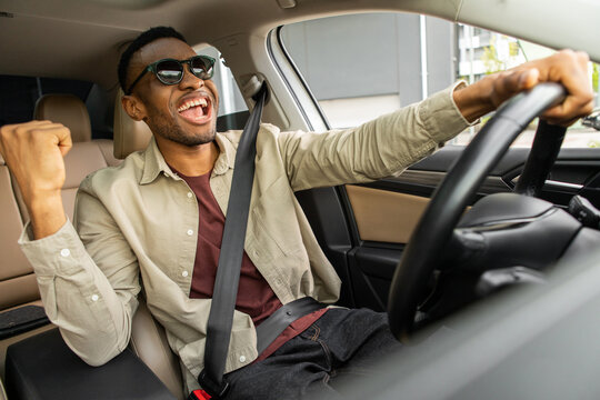A joyful African American in glasses dances in a car, sings while driving his car. Road fun