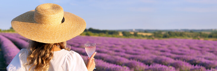 Beautiful young woman drinking wine in lavender field