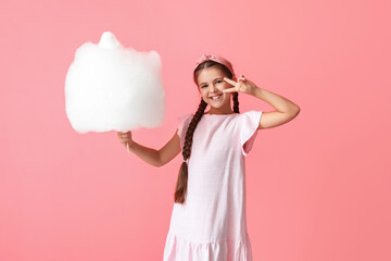 Cute little girl with cotton candy on pink background