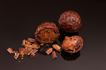 round chocolate sweets with soft chocolate filling, with a large scattering of chocolate, lying on a black glass with reflection.