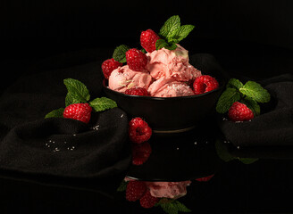 raspberry pink ice cream in a black bowl on a black background with raspberries and mint leaves