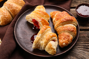 Plate of delicious croissants with raspberry jam on wooden background