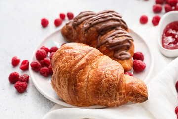 Plate of delicious croissants with raspberries on light background