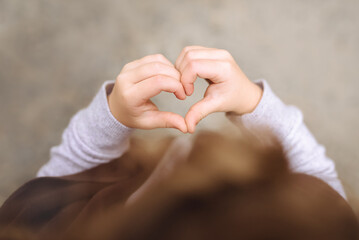 Close up of baby making heart shape with his hands on gray background. A sign of love and happiness